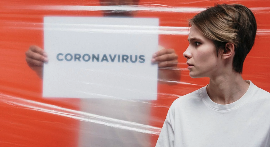 Concerned young woman looks at a coronavirus sign behind a plastic sheet