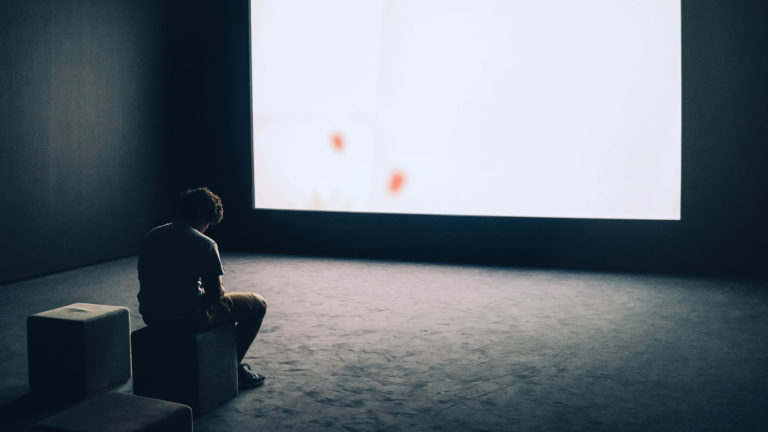 An individual with a pornography addiction sits dejectedly in front of a large video screen